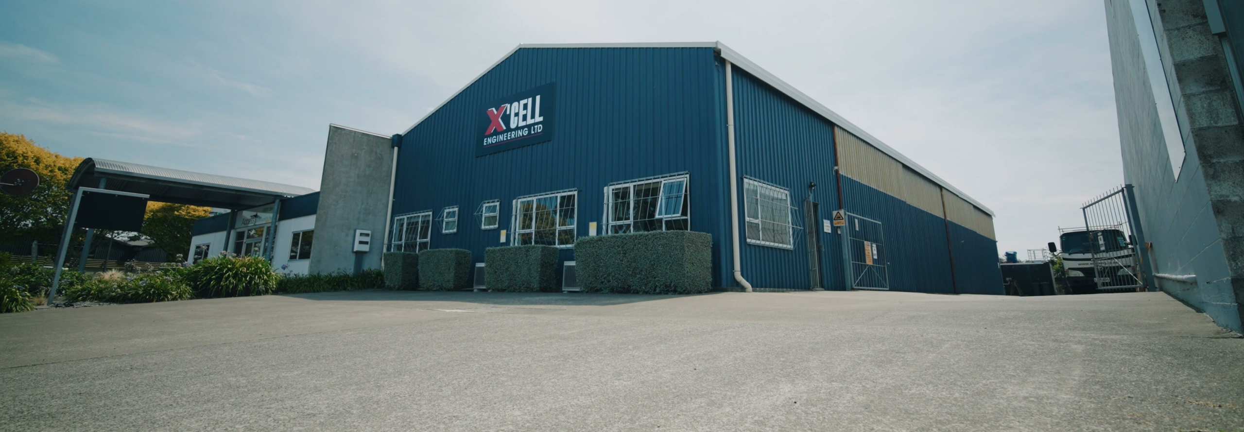 about-hero A wide view of the X'Cell Engineering Ltd industrial building with its navy blue facade and logo, under a clear sky.